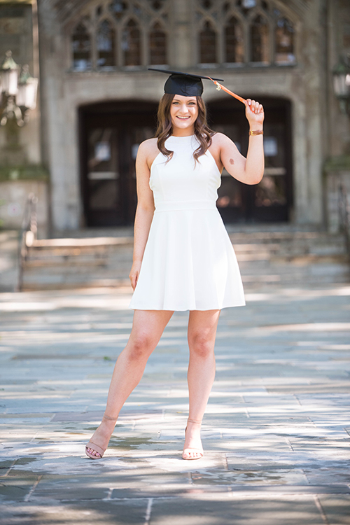 Alexis Roberts in grad cap and white dress on law quad during a sunny day