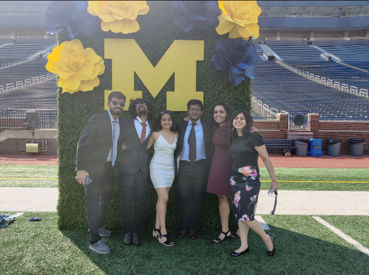 group of students stand in front of block M and giant Maize and Blue flowers
